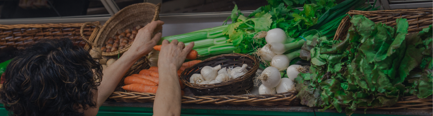 Persona agafant pastanagues en un mercat amb cistelles de verdures fresques
