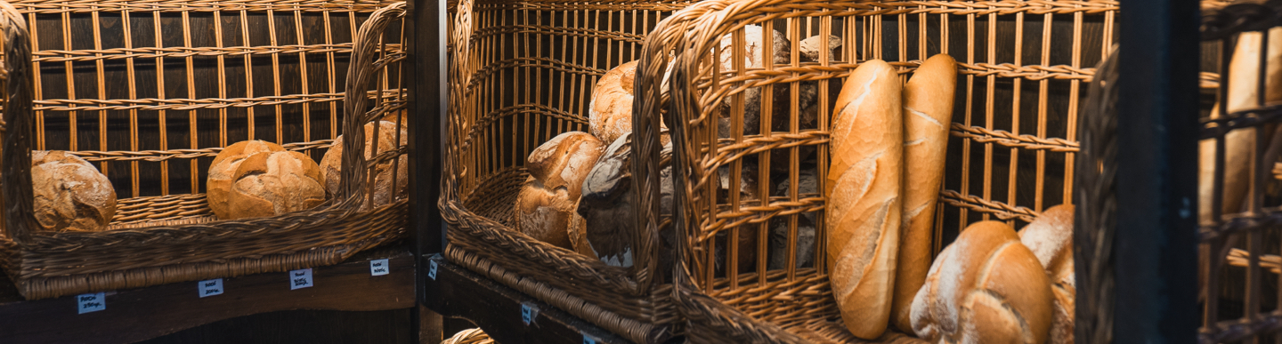 Pans artesans (barres i rodons) en cistells de vímet amb etiquetes de preu.