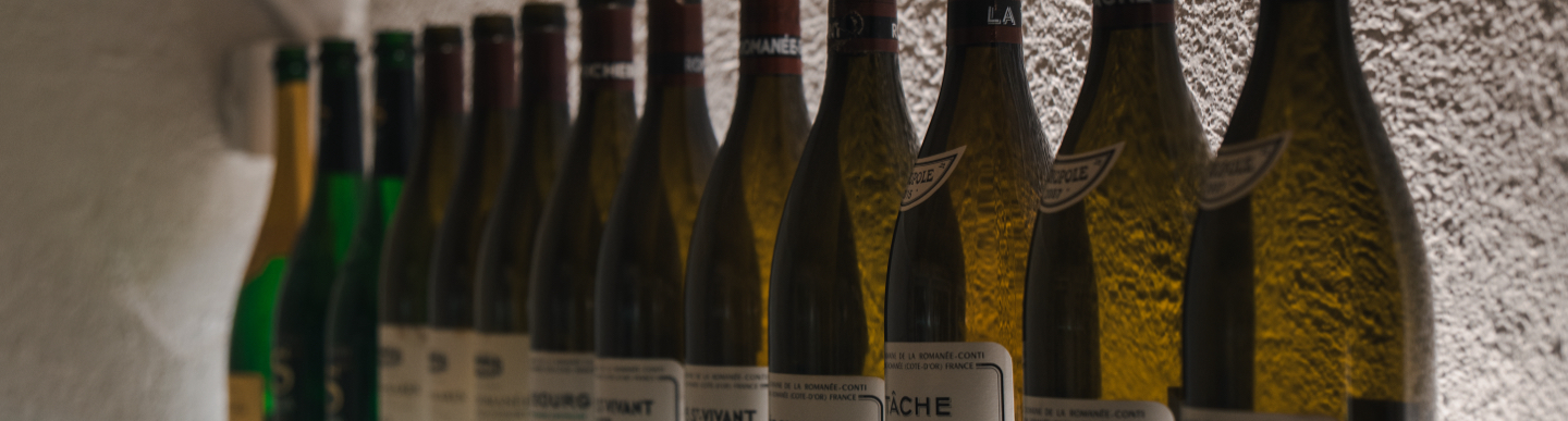 Ampolles de vi allargades en prestatge davant paret texturada.